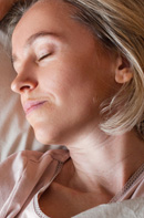 Close-up of a woman with short gray hair resting with eyes closed in soft light, conveying calm.