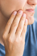 Close-up of a person touching their lower cheek or jaw with fingers, suggesting discomfort or contemplation.